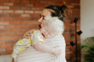 A mother gently holds her crying baby indoors, capturing a tender moment.